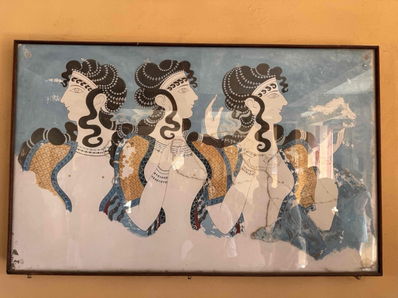 Reproduction of a famous Minoan fresco at Knossos, showing elaborately dressed women with elegant hairstyles and ceremonial gestures.